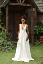 Woman in an ivory wedding dress standing outdoors near a wooden structure.
