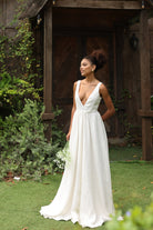 Woman in an ivory wedding dress standing outdoors with greenery around