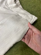 Close-up of a hand holding beige pants on a green surface