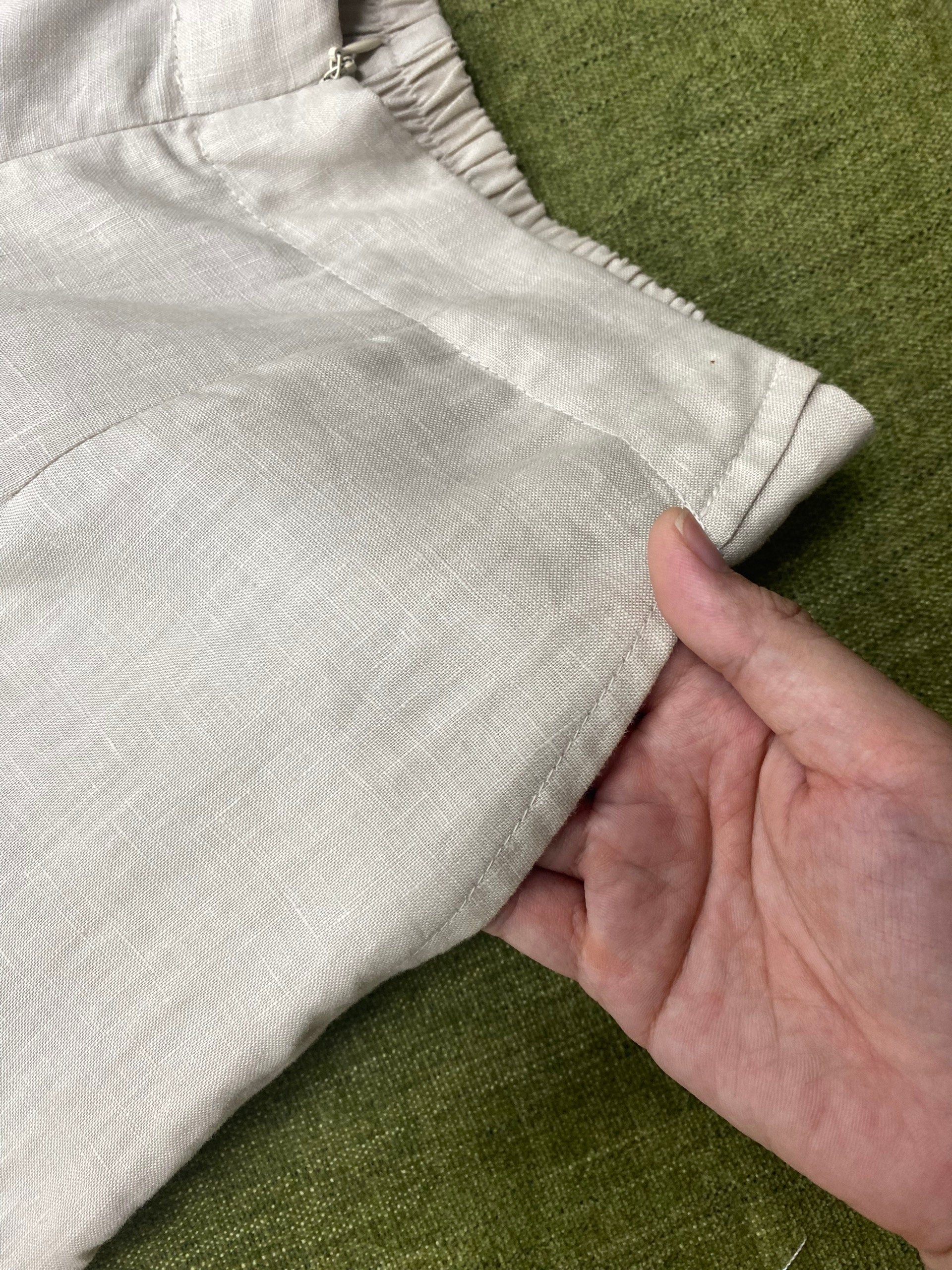 Close-up of a hand holding beige pants on a green surface