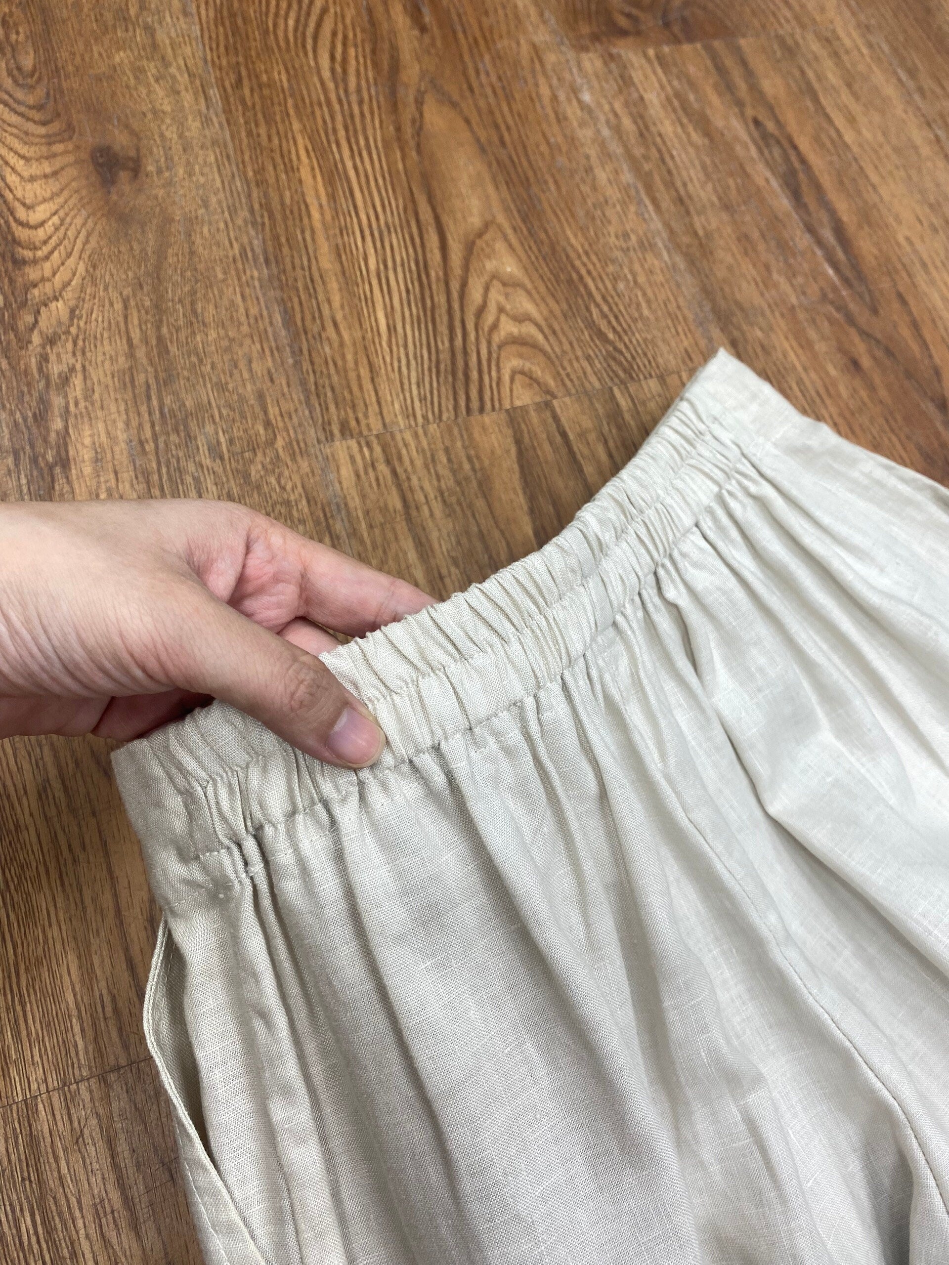 Beige pants with a hand adjusting the waistband on a wooden floor.