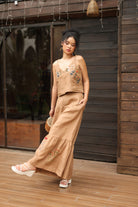 Woman in a beige outfit with floral details standing in front of a wooden wall.