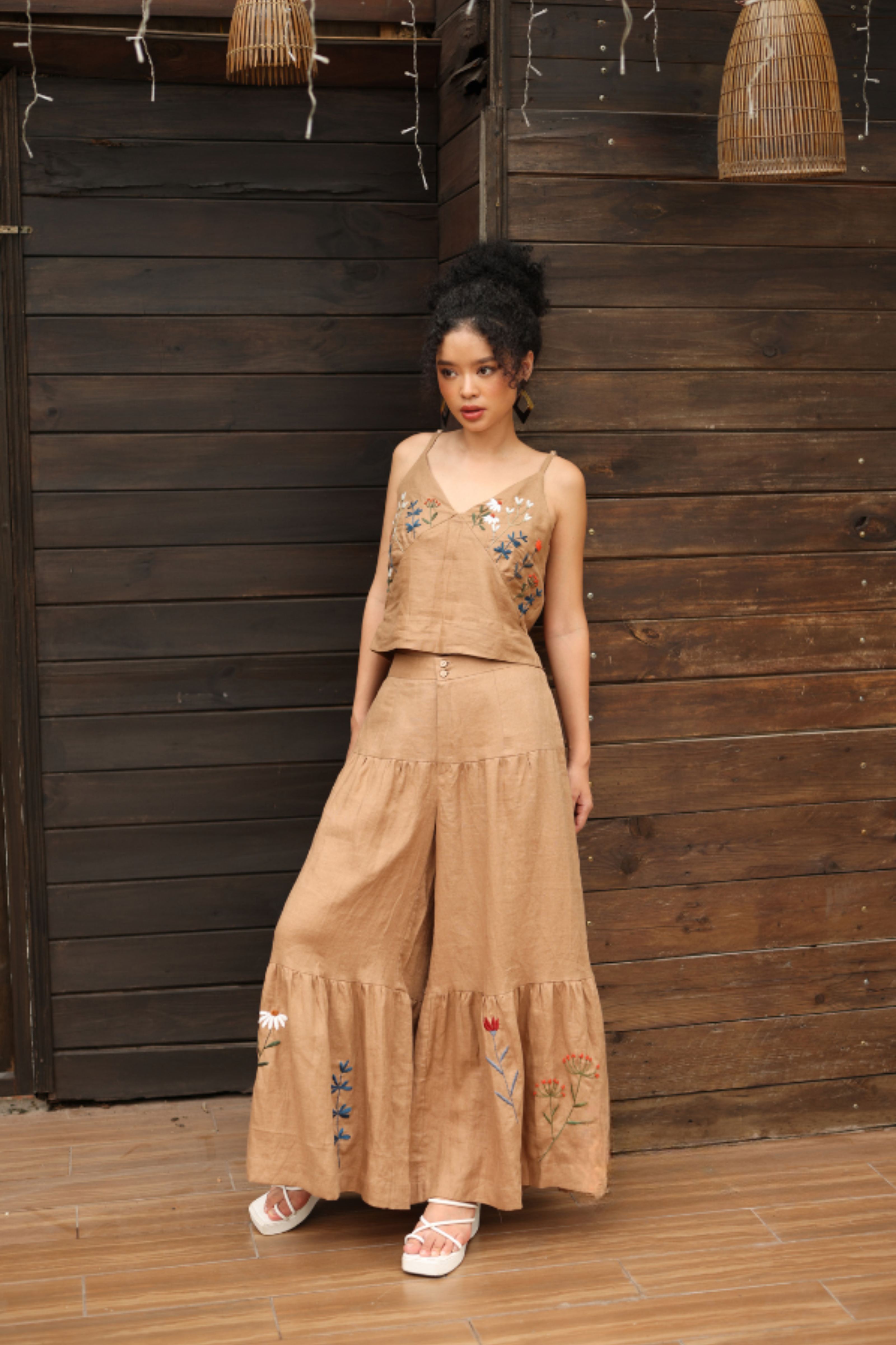 Woman wearing a beige embroidered outfit standing against a wooden wall.