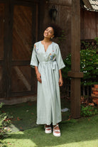 Woman in a light green dress standing outdoors near a wooden building.