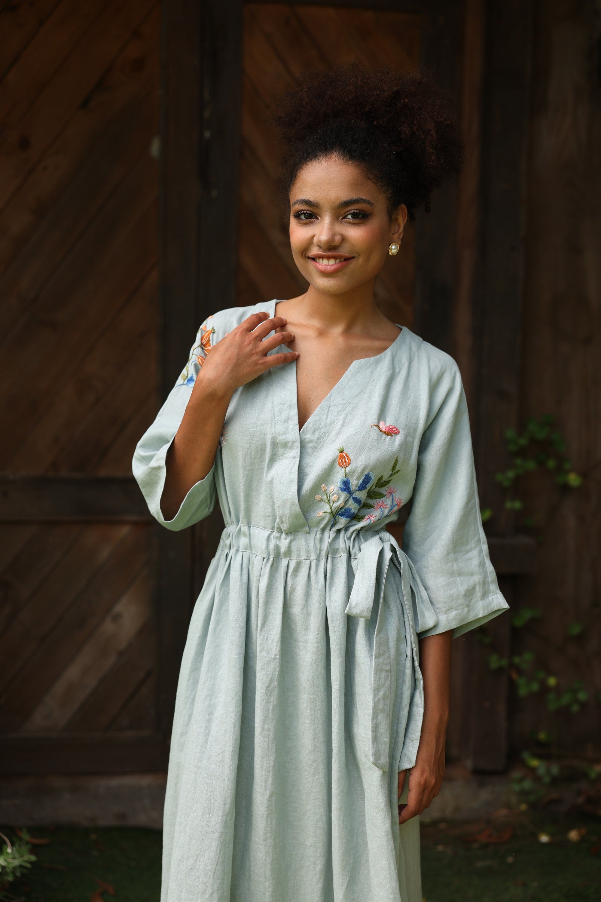 Woman wearing a light green dress with floral embroidery against a wooden background
