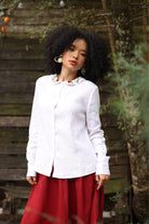 Woman wearing a white blouse with floral details and a red skirt outdoors.