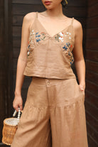 Woman wearing a beige embroidered top and wide-leg pants against a dark background