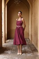 Woman in a burgundy dress standing in an arched stone corridor.