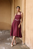 Woman in a burgundy dress standing against a beige wall.