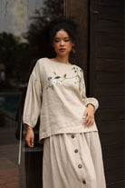 Woman wearing a beige outfit with floral embroidery standing outdoors.