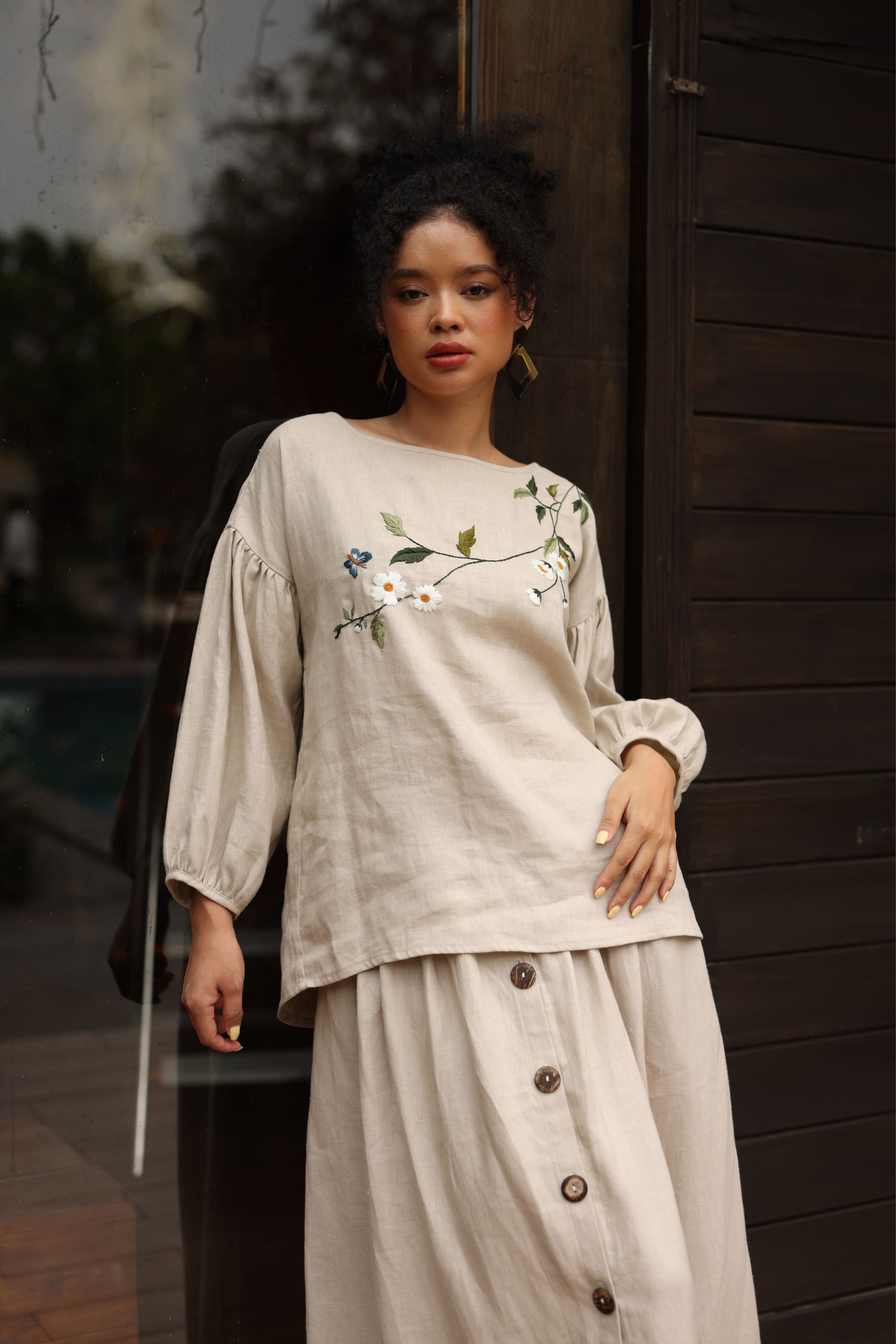 Woman wearing a beige outfit with floral embroidery standing outdoors.