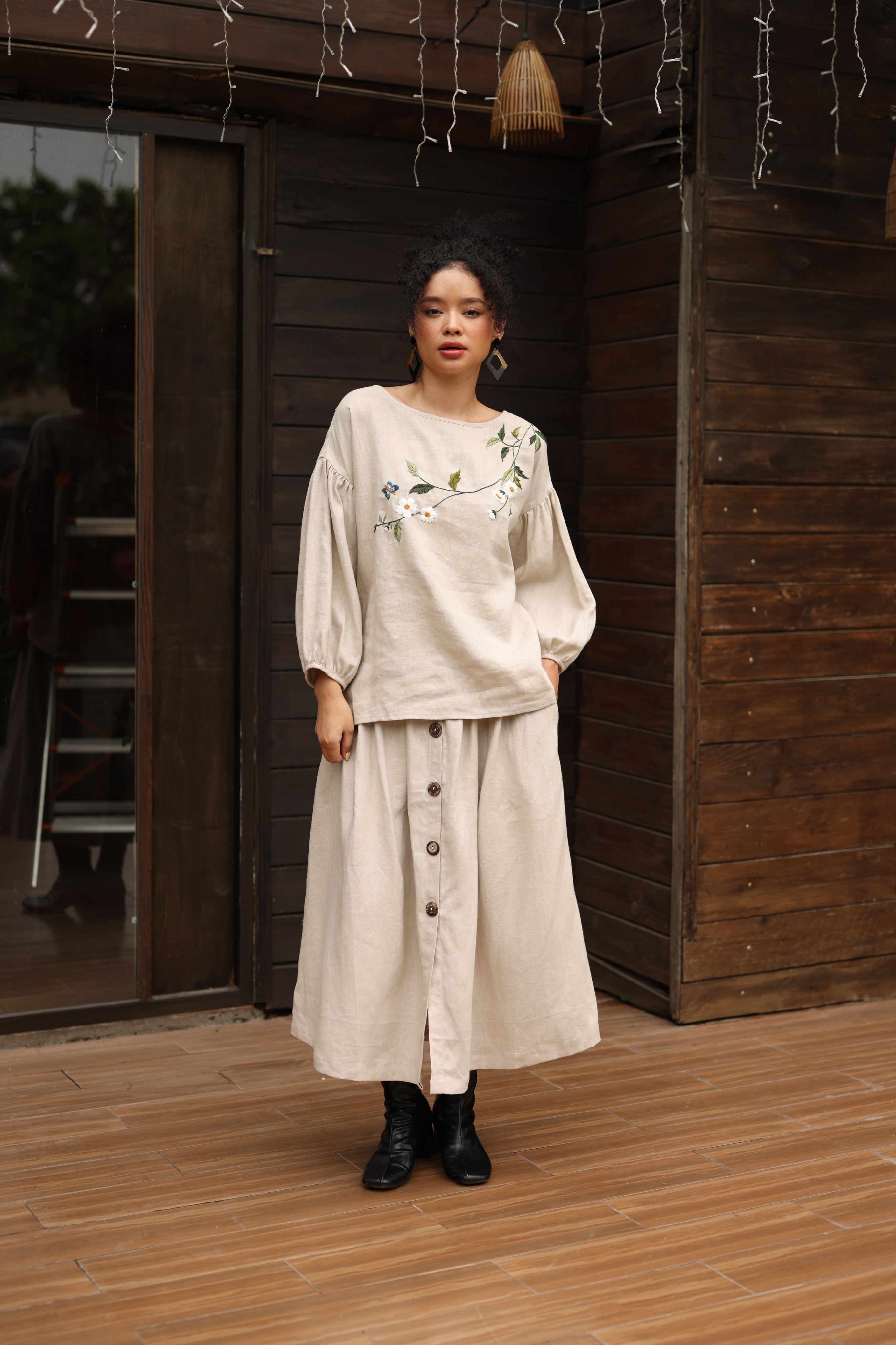 Woman wearing a beige outfit with floral details in front of a wooden wall.