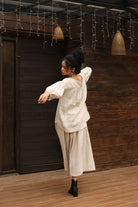 Woman in an outfit standing in a room with wooden walls and hanging baskets.