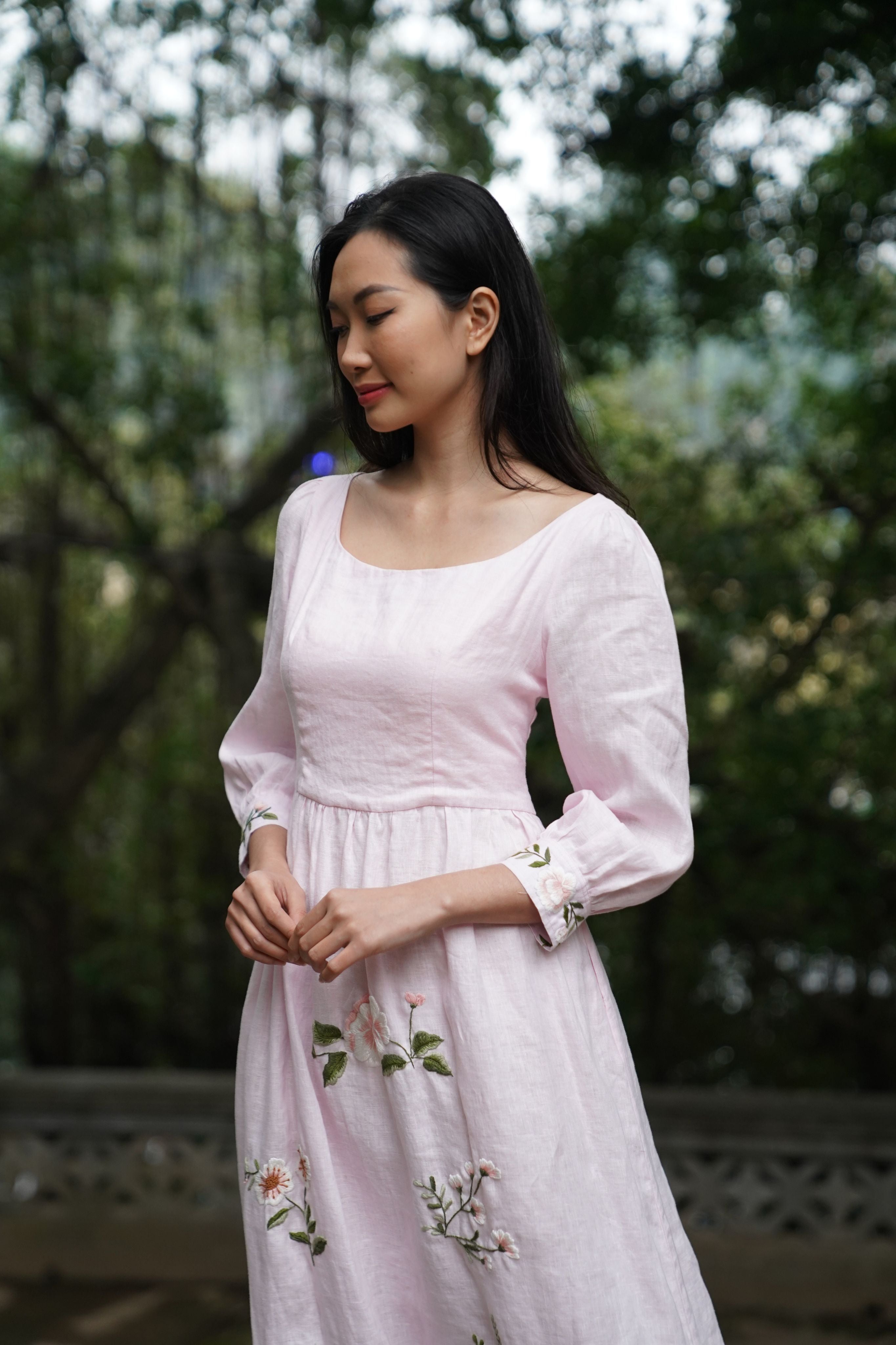 Woman wearing a light pink dress with floral embroidery in an outdoor setting