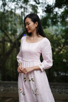 Woman wearing a light pink dress with floral embroidery in an outdoor setting