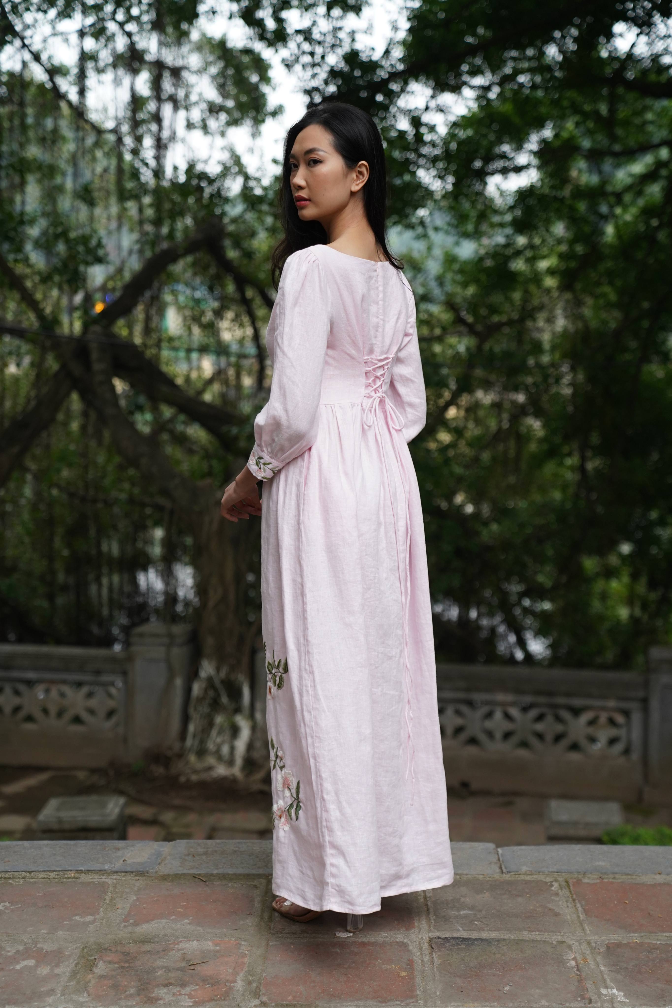 Woman in a long, light-colored dress standing outdoors with trees in the background