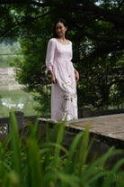 Woman in a floral dress standing outdoors with greenery around