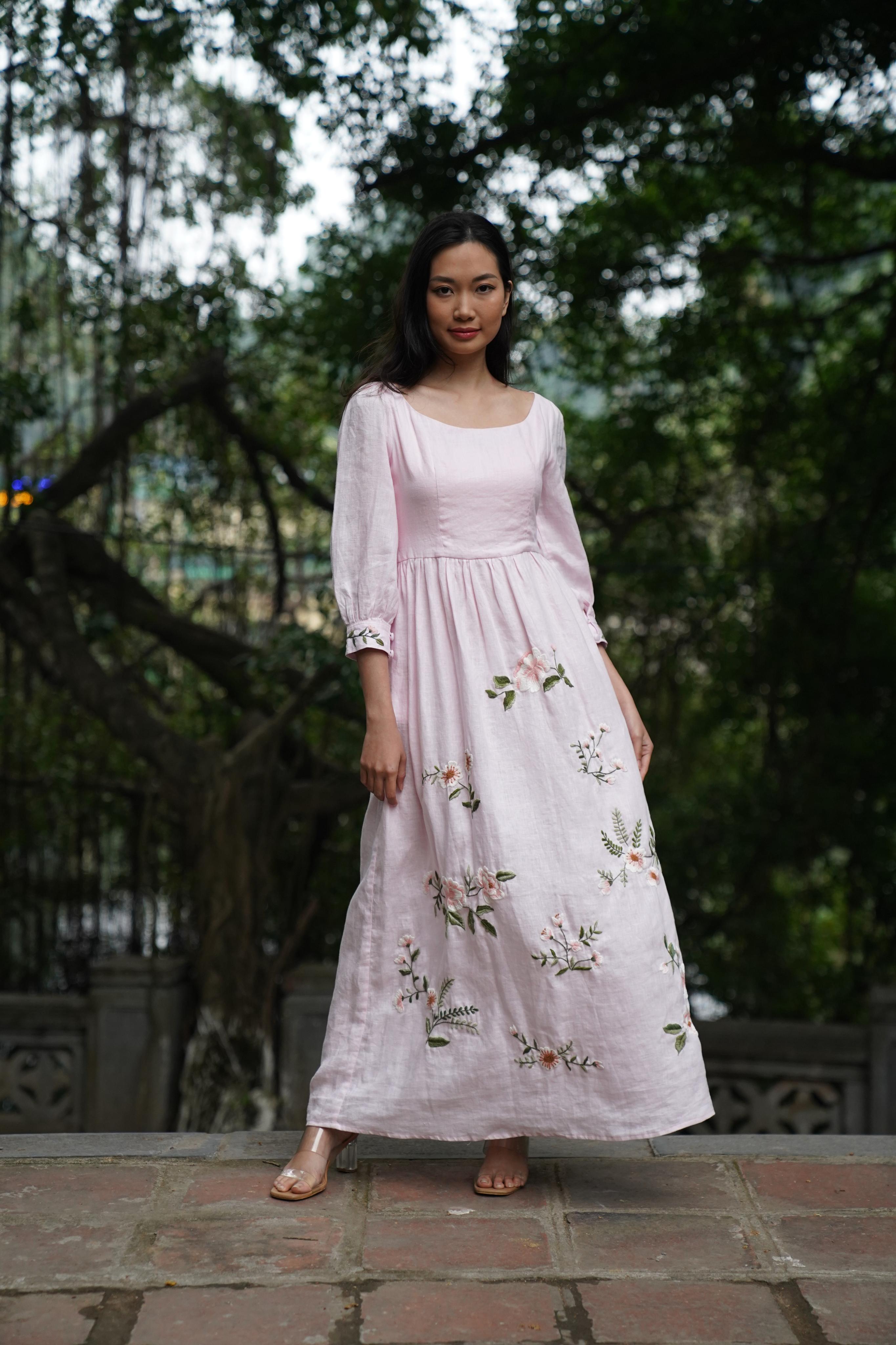Woman wearing a light pink dress with floral embroidery standing outdoors.