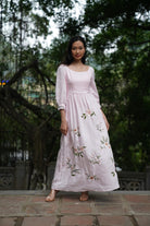 Woman wearing a light pink dress with floral embroidery standing outdoors.
