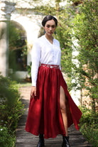 Woman in a white blouse and red skirt standing outdoors with greenery around