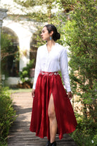 Woman in a white blouse and red skirt standing on a wooden path with greenery around.
