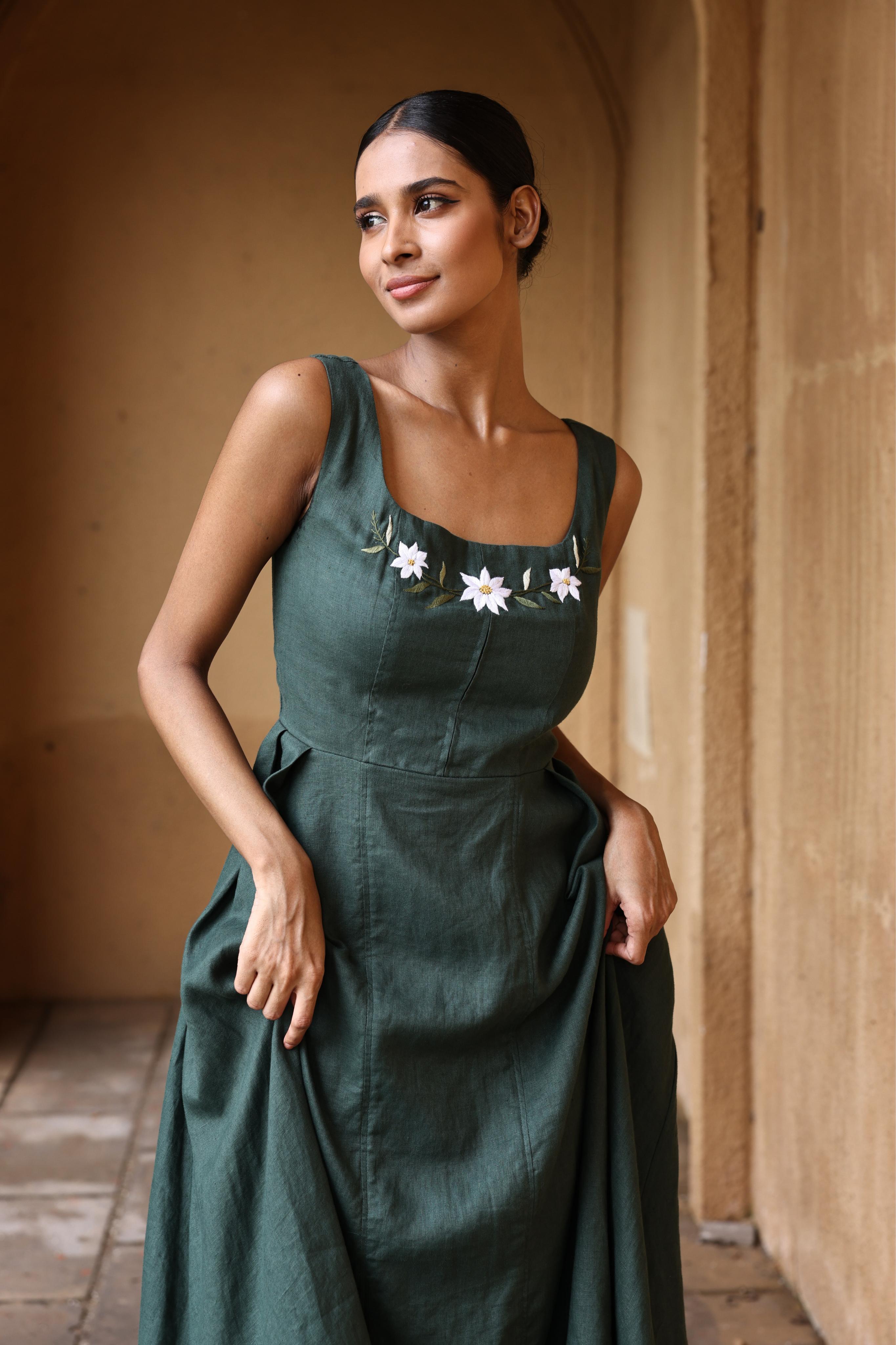 Woman wearing a dark green dress with floral details in an arched doorway.
