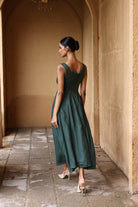 Woman in a green dress standing in an arched hallway with beige walls.