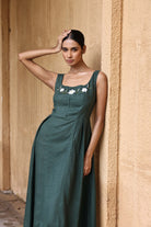 Woman in a green dress with floral details against a beige wall