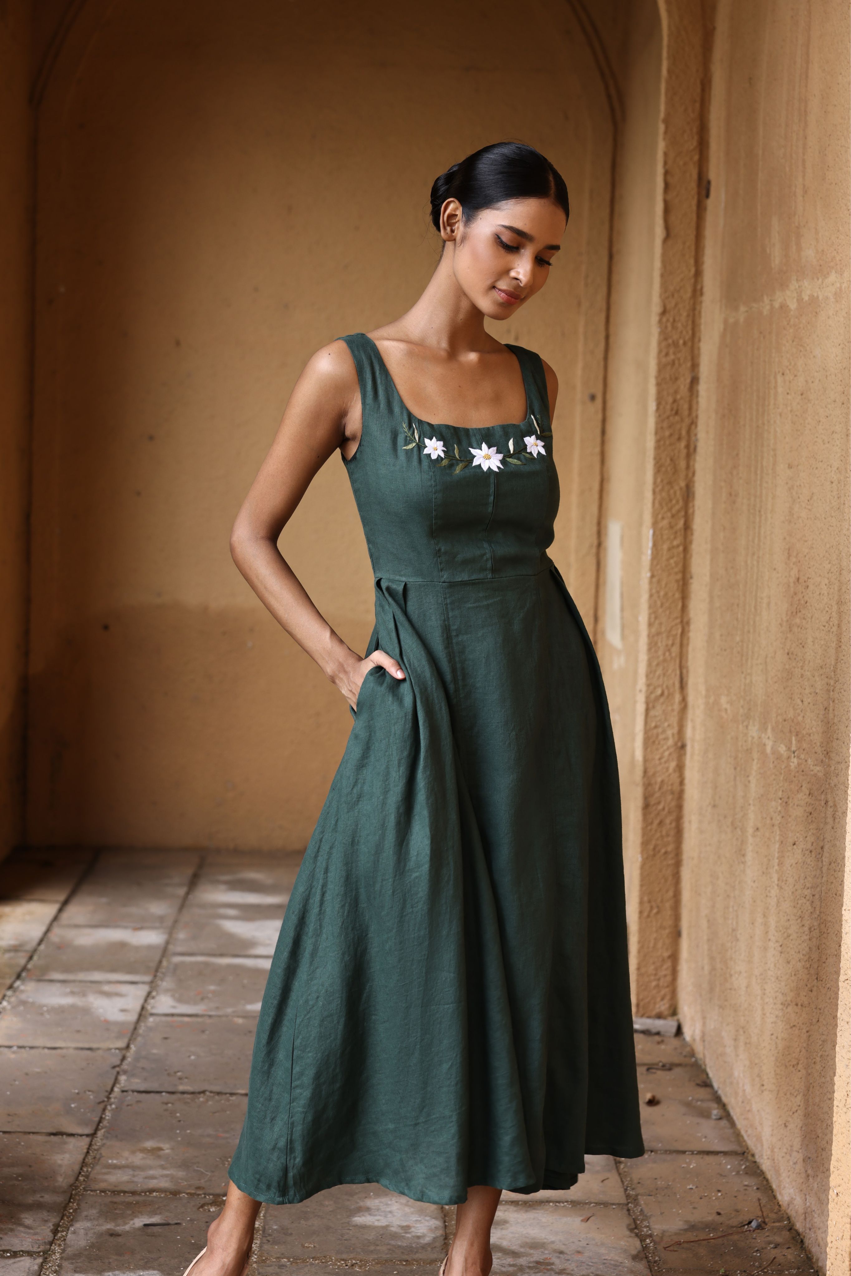 Woman wearing a green dress with floral embroidery in an arched hallway.