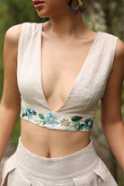 Woman wearing a beige sleeveless top with floral embroidery against a blurred natural background