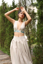 Woman in a top with floral details and beige skirt standing outdoors with trees in the background