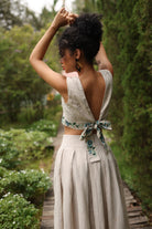 Woman in a light-colored outfit with floral details standing in a garden.