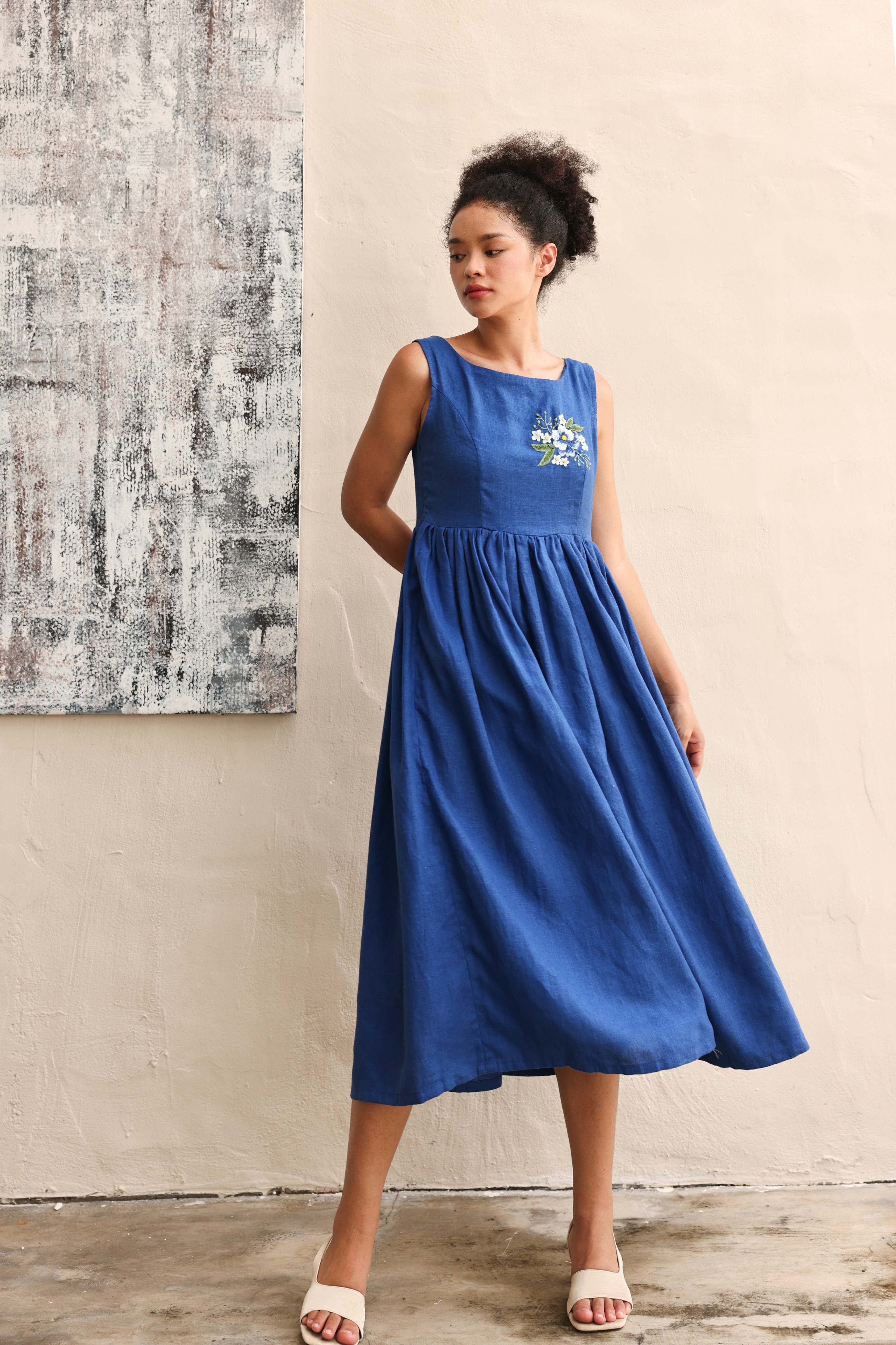 Woman wearing a blue dress standing against a textured wall.