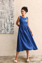 Woman wearing a blue dress standing against a textured wall.