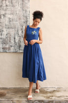 Woman wearing a blue dress standing against a textured wall.