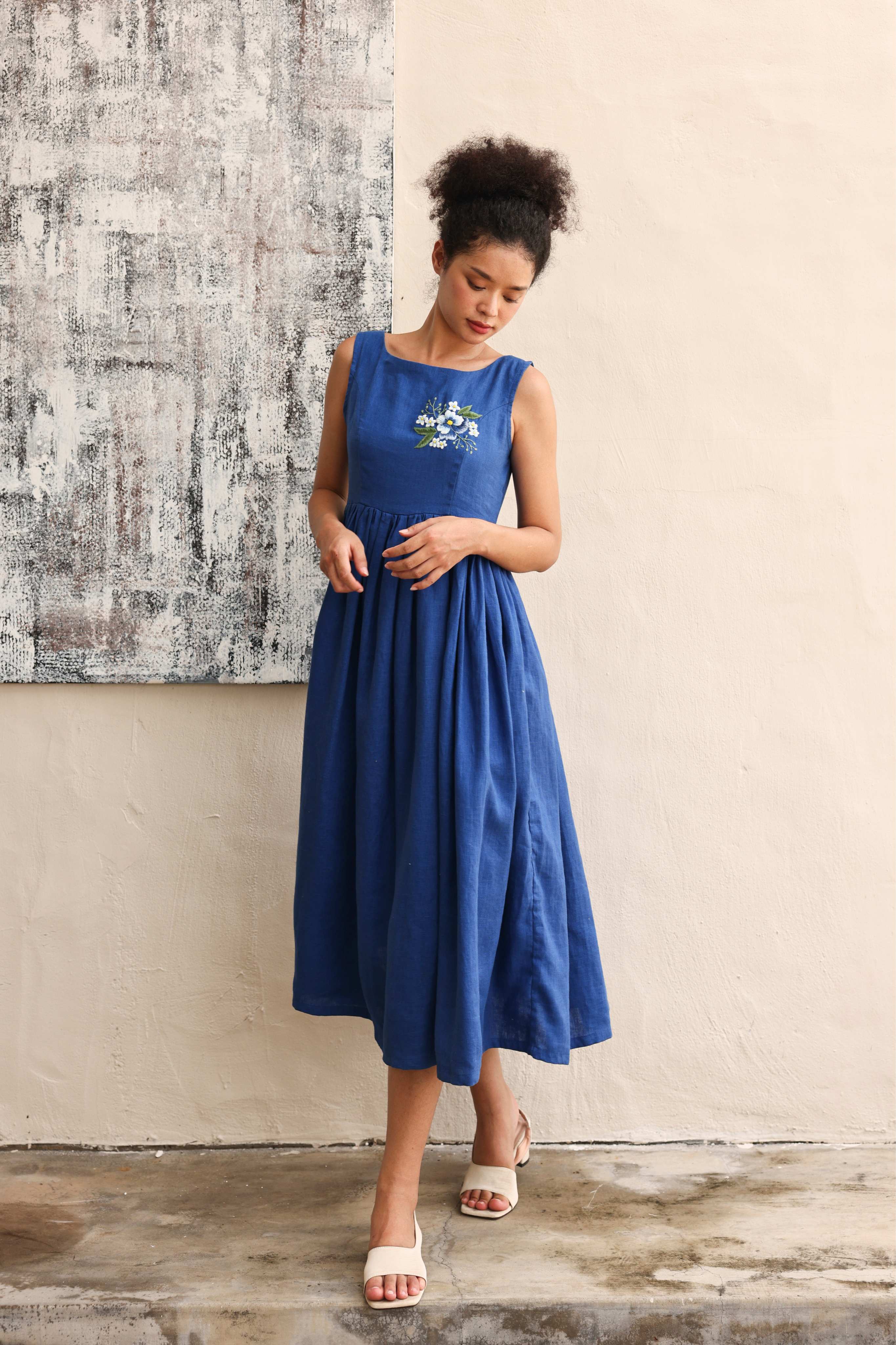 Woman wearing a blue dress standing against a textured wall.