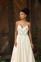 Woman wearing a floral embroidered dress standing in front of wooden doors.