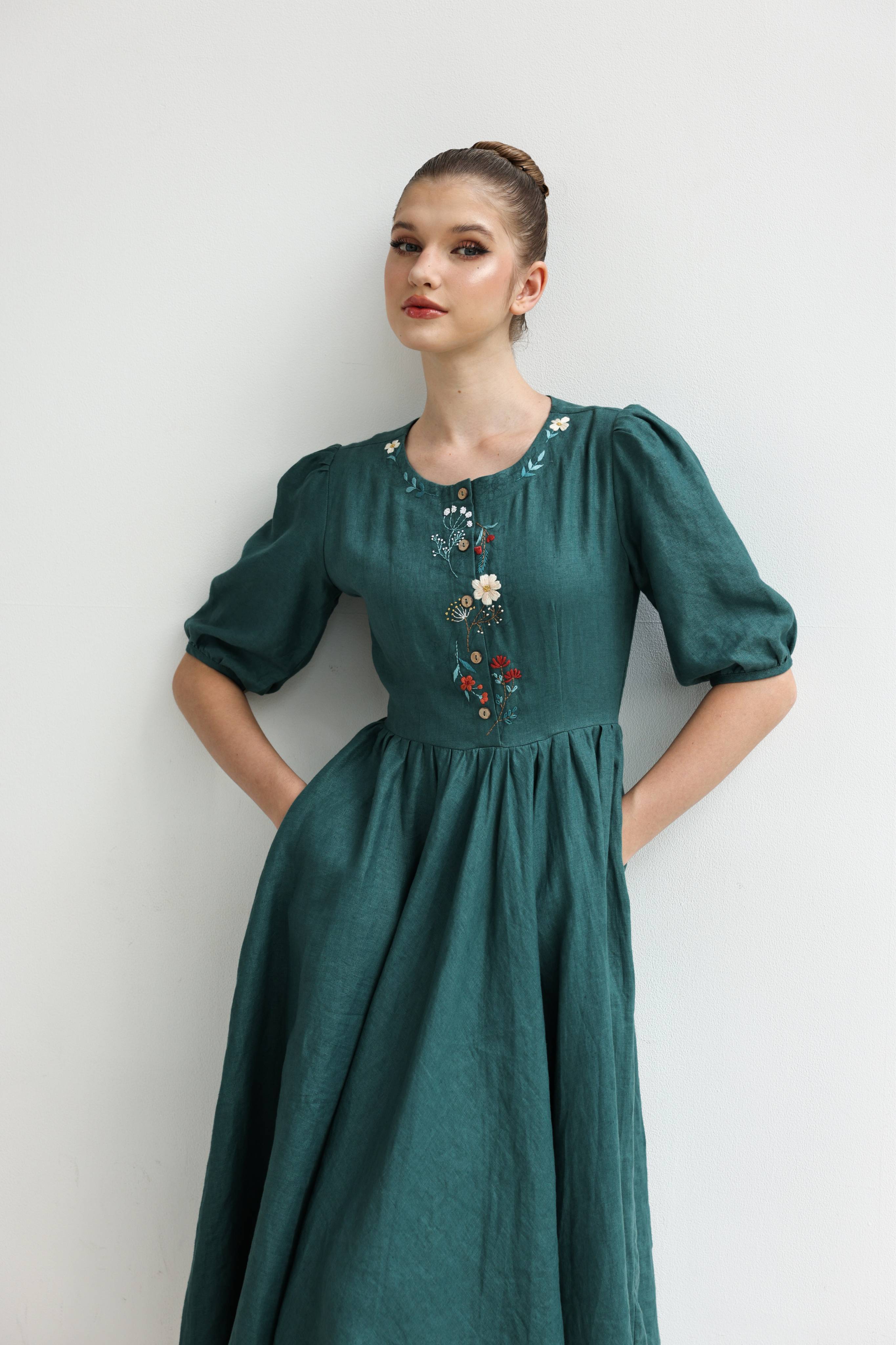 Woman wearing a green dress with floral embroidery against a white background