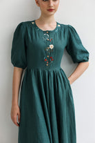 Woman wearing a green dress with floral embroidery on a plain background