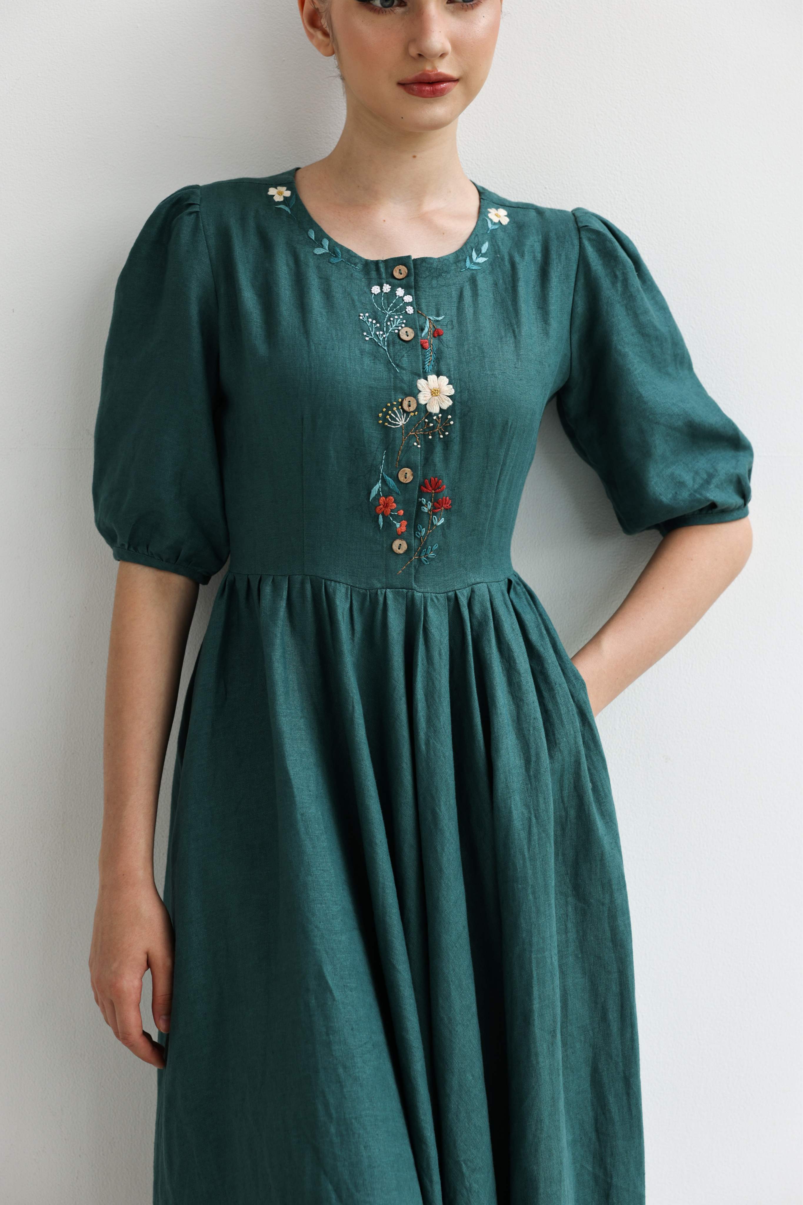 Woman wearing a green dress with floral embroidery on a plain background
