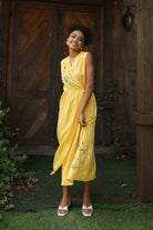 Woman in a yellow dress standing in front of a wooden door.