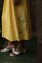 Yellow dress with floral embroidery worn by a person on a grassy background