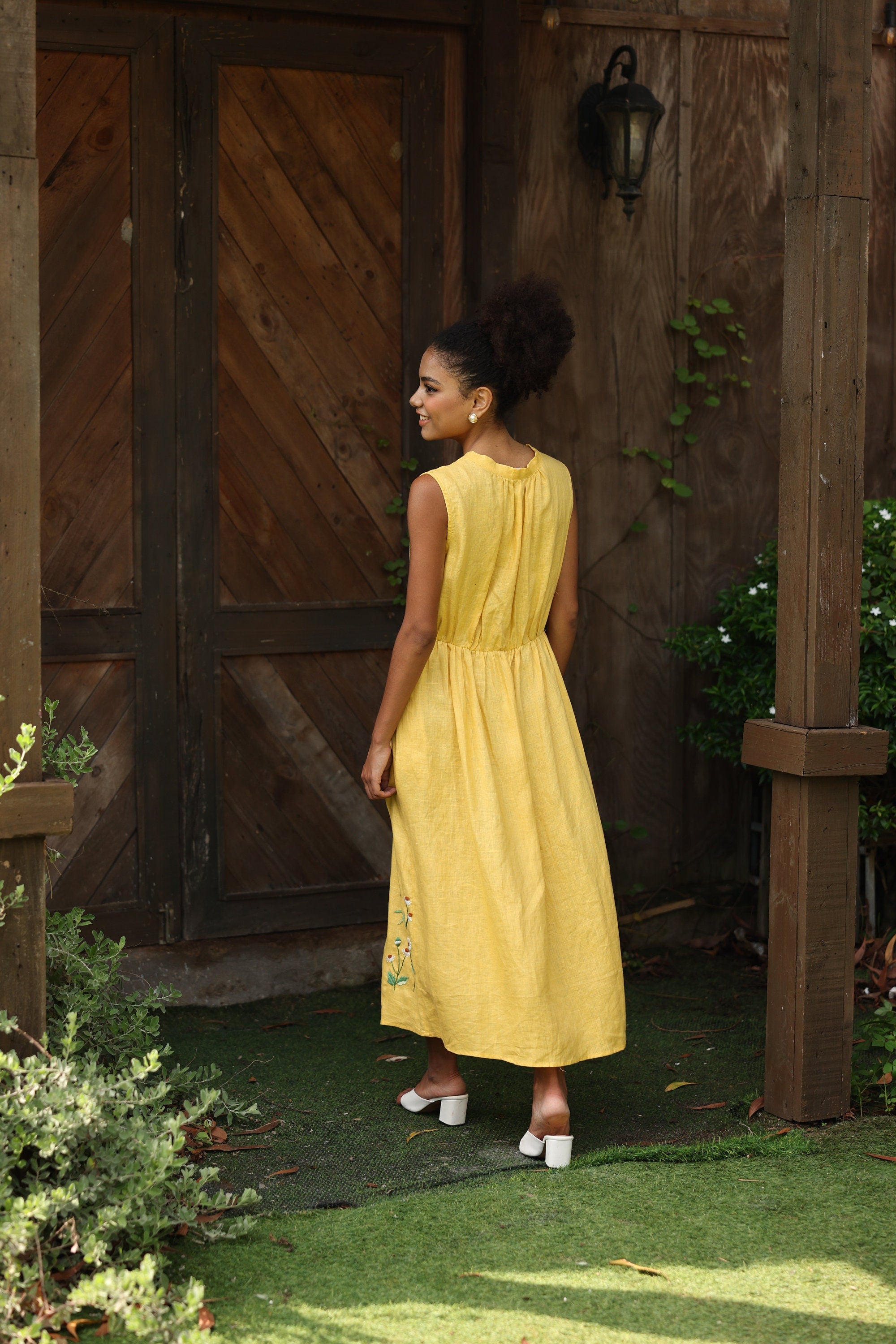 Woman in a yellow dress standing in front of a wooden door with plants around.