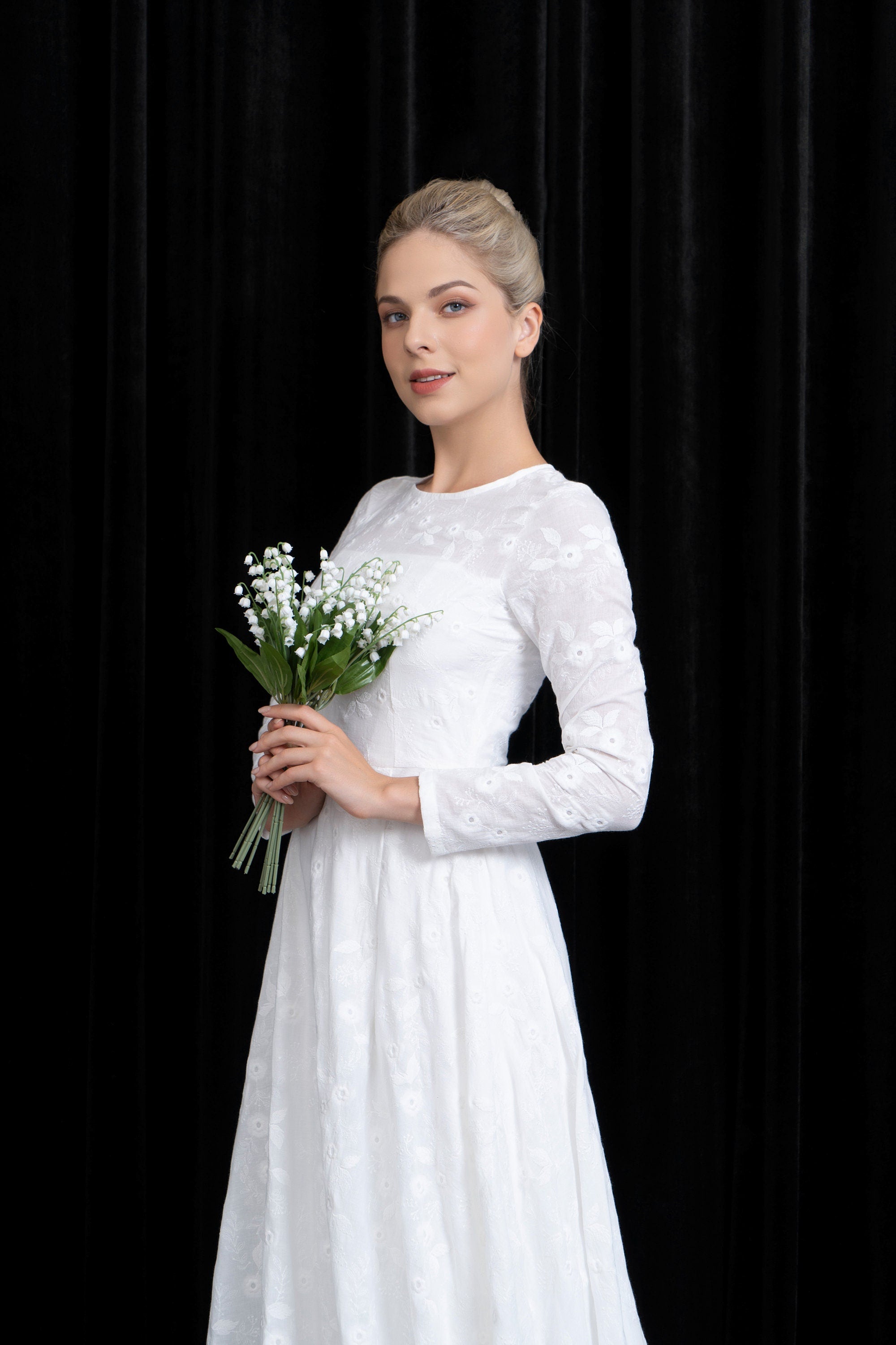 Woman in a white dress holding flowers against a black background