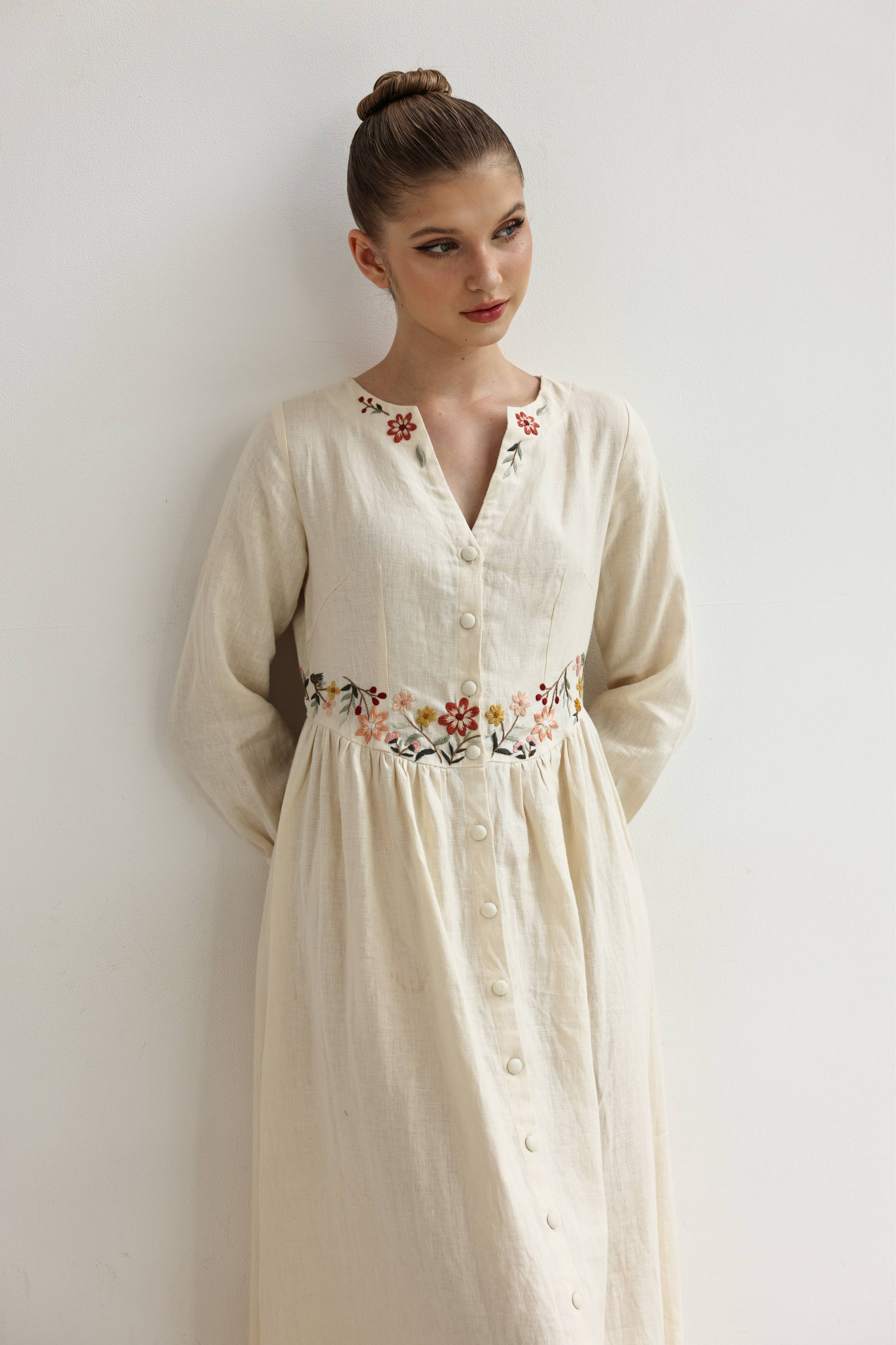 Woman wearing a cream-colored dress with floral embroidery against a plain background