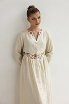 Woman wearing a cream-colored dress with floral embroidery against a plain background