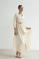 Woman wearing a long, light-colored dress with floral embellishments on a plain background