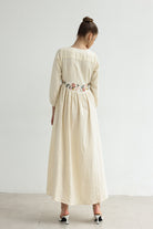 Woman wearing a long dress with floral embroidery on a white background