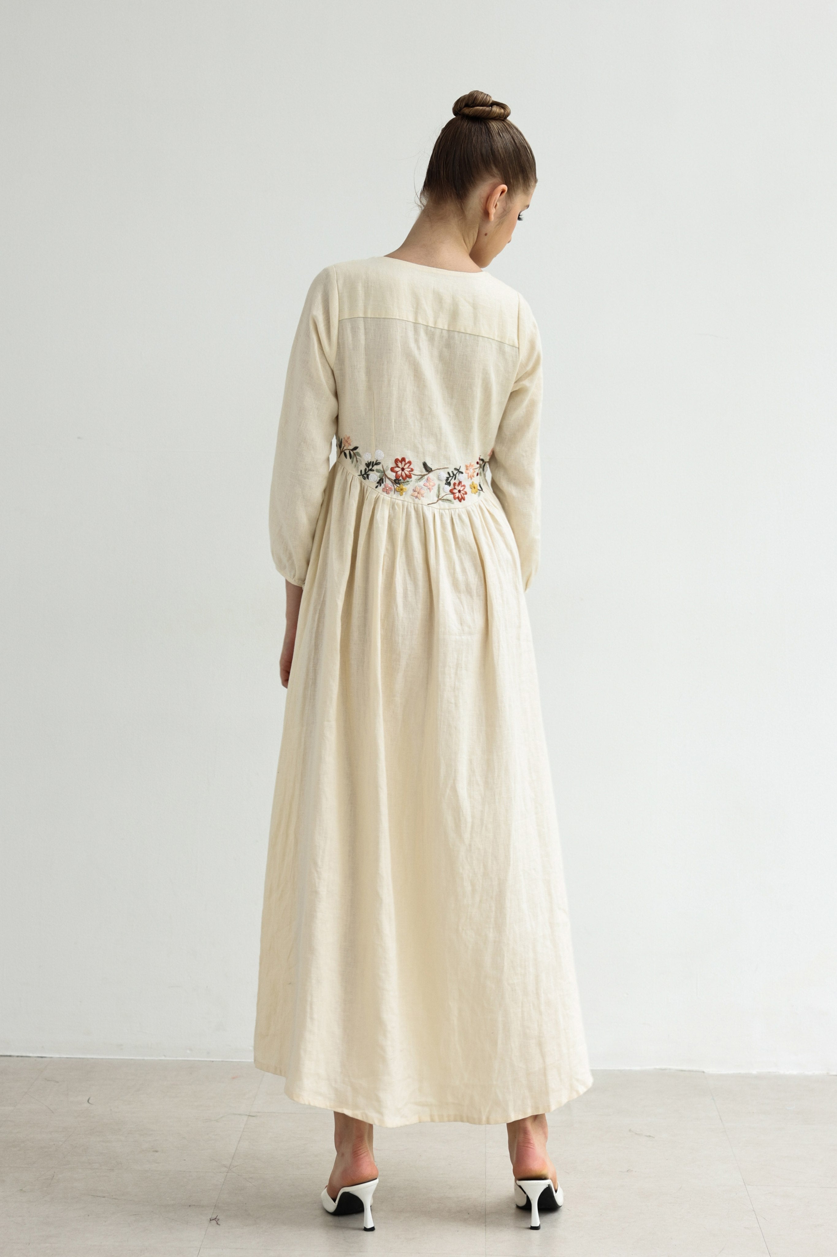 Woman wearing a long dress with floral embroidery on a white background