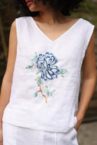 White sleeveless top with blue floral embroidery on a blurred background